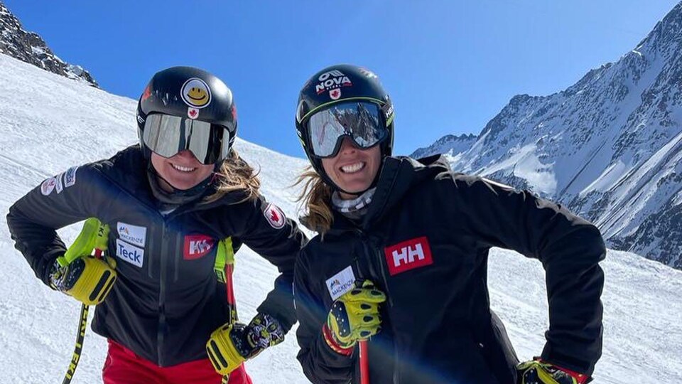 Deux skieuses souriantes posent pour la photo, en combinaison de vitesse, sur une pente de ski enneigée. 