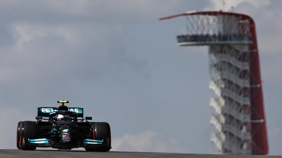 Une monoplace de F1 roule sur un circuit, il y a une tour d'observation au loin.