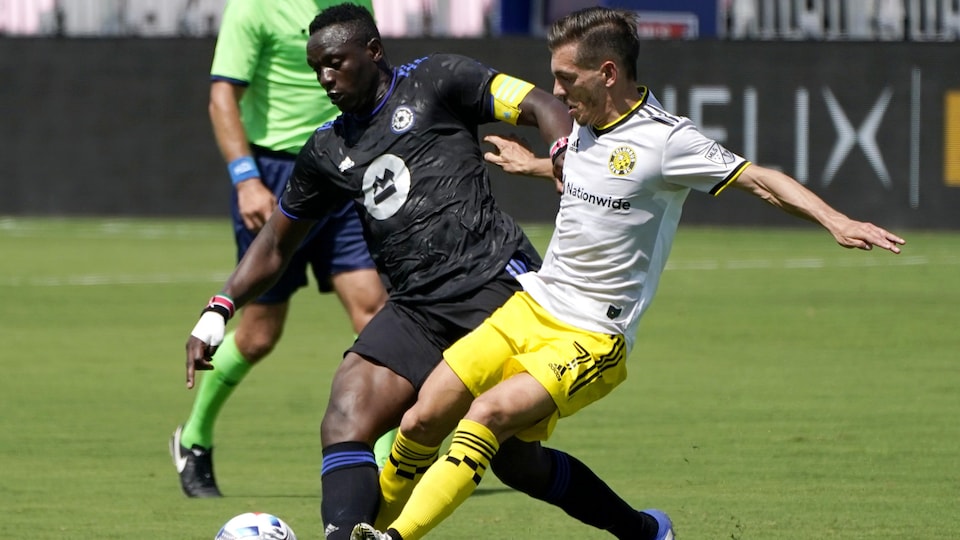 Deux joueurs de soccer se disputent le ballon en milieu de terrain.