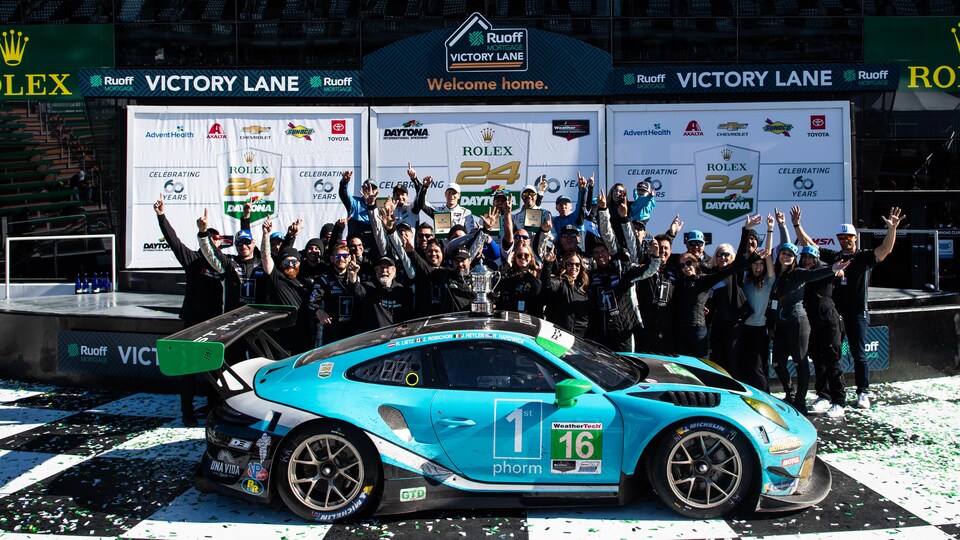 A motor racing team celebrates the victory of its driver in front of his car.