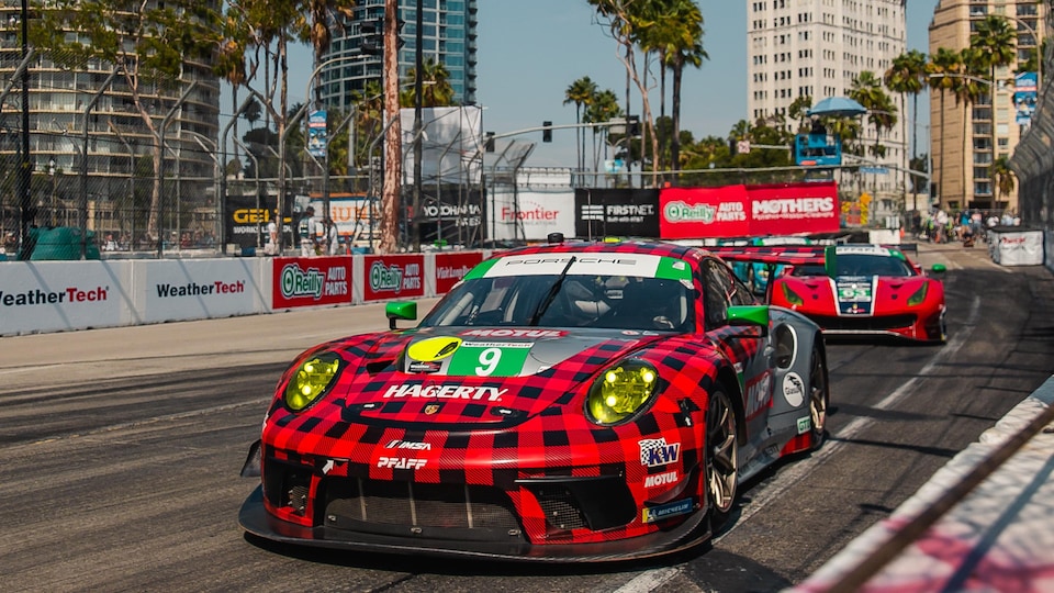 Porsche vehicles are driving on a racing circuit during an event. 