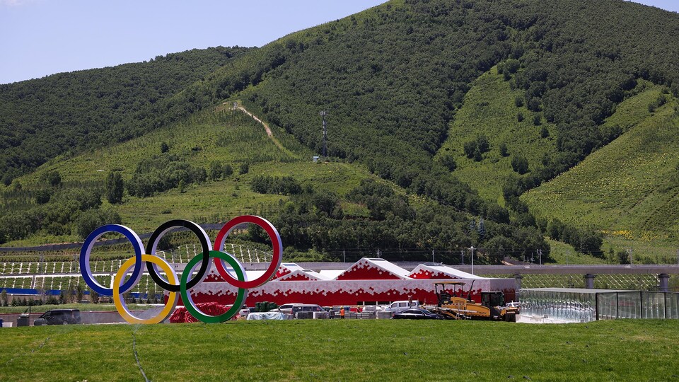 Des chalets de couleur rouge situ&eacute;s devant des montagnes vertes de m&ecirc;me qu'une sculpture repr&eacute;sentant les anneaux olympiques.