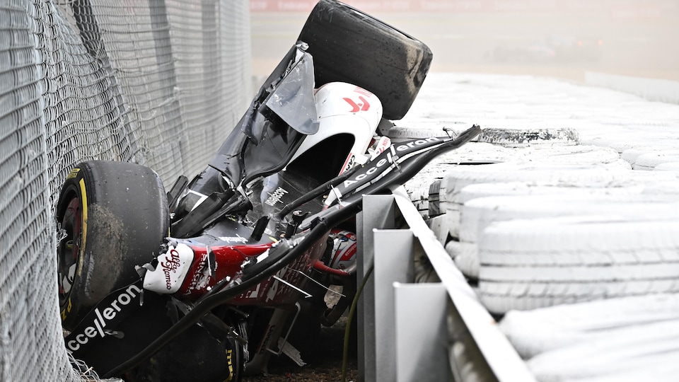 L'épave de la voiture Alfa Romeo, rouge et blanche, est renversée, coincée entre une clôture et le muret de pneus. Zhou est sous la voiture. 