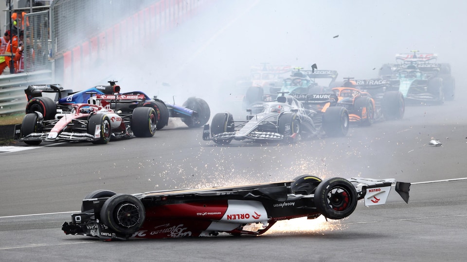 L'Alfa Romeo rouge et blanche de Zhou, à l'envers, glisse en faisant une pluie d'étincelles, alors que derrière, un nuage de fumée cache le peloton de voitures au premier virage du Grand Prix.