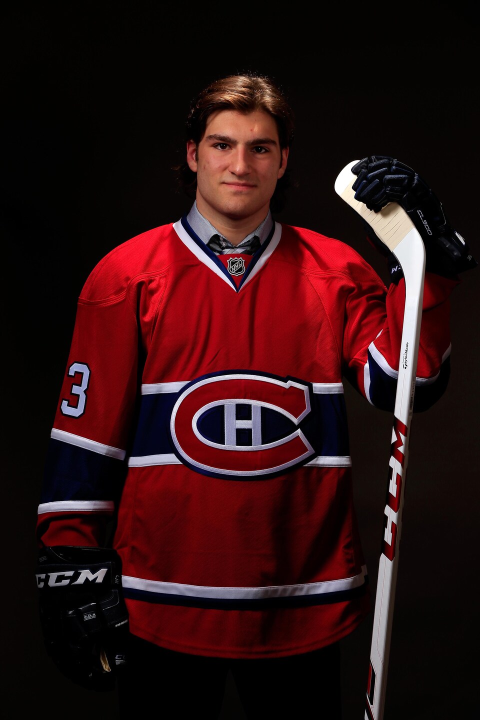 A hockey player, wearing a blue, white and red Montreal Canadiens jersey, posed while holding the blade of his stick in his left hand. 