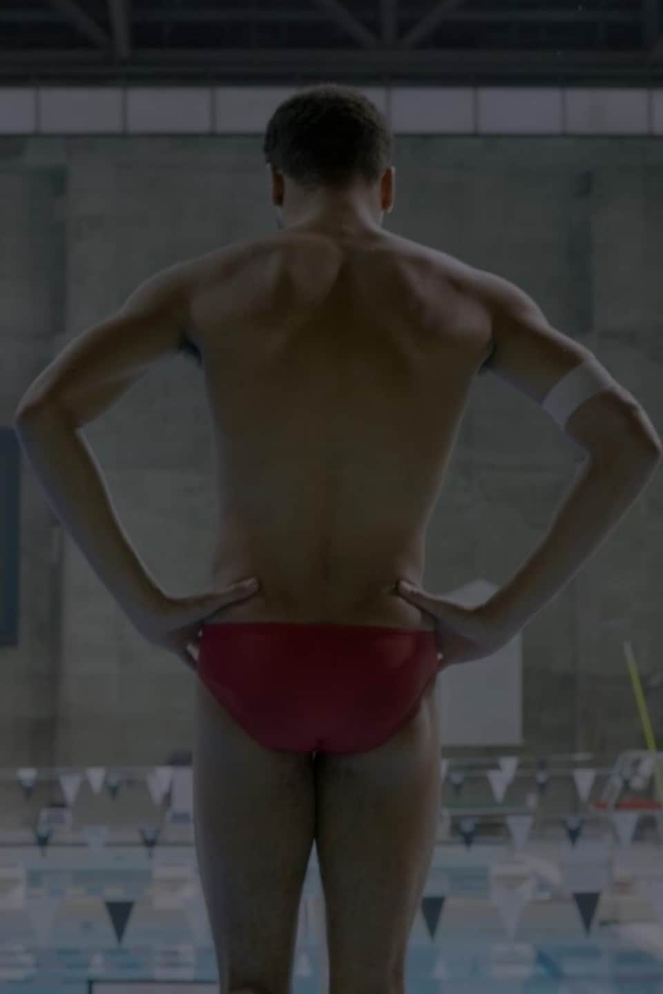 Un plongeur de dos dans un maillot rouge au bout d'un tremplin.