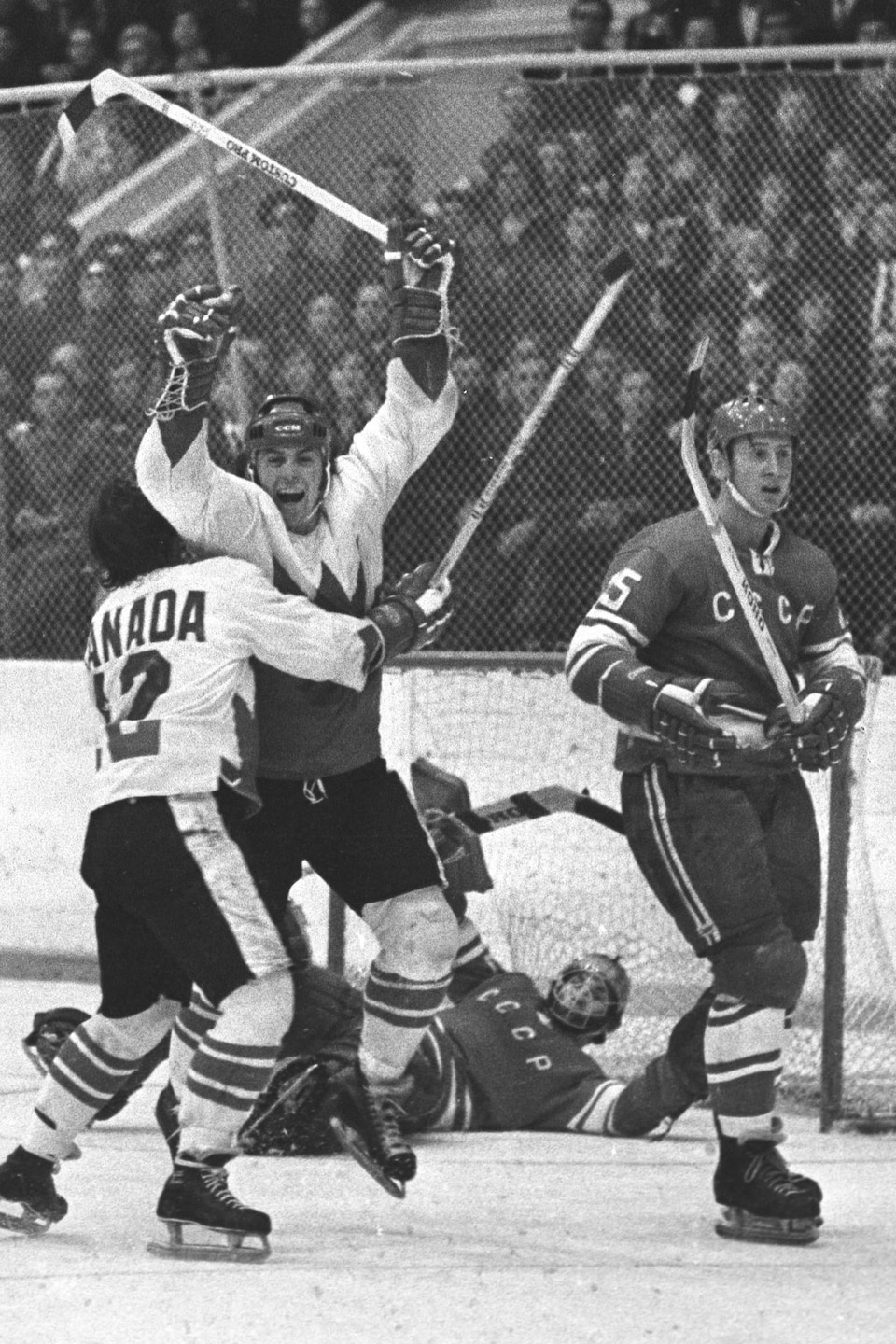 Photo en noir et blanc d'un joueur de hockey qui serre dans ses bras un coéquipier qui lève les bras en l'air. 