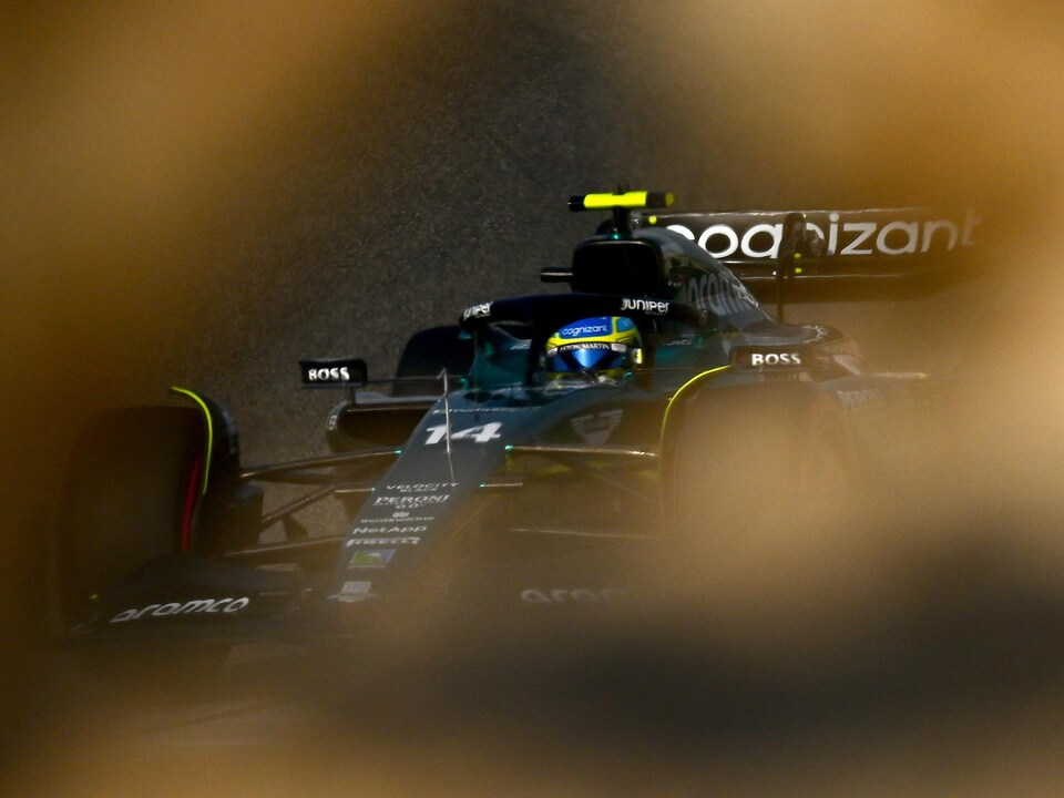 Il roule sur un circuit au milieu du désert, on voit des rochers en avant-plan. 