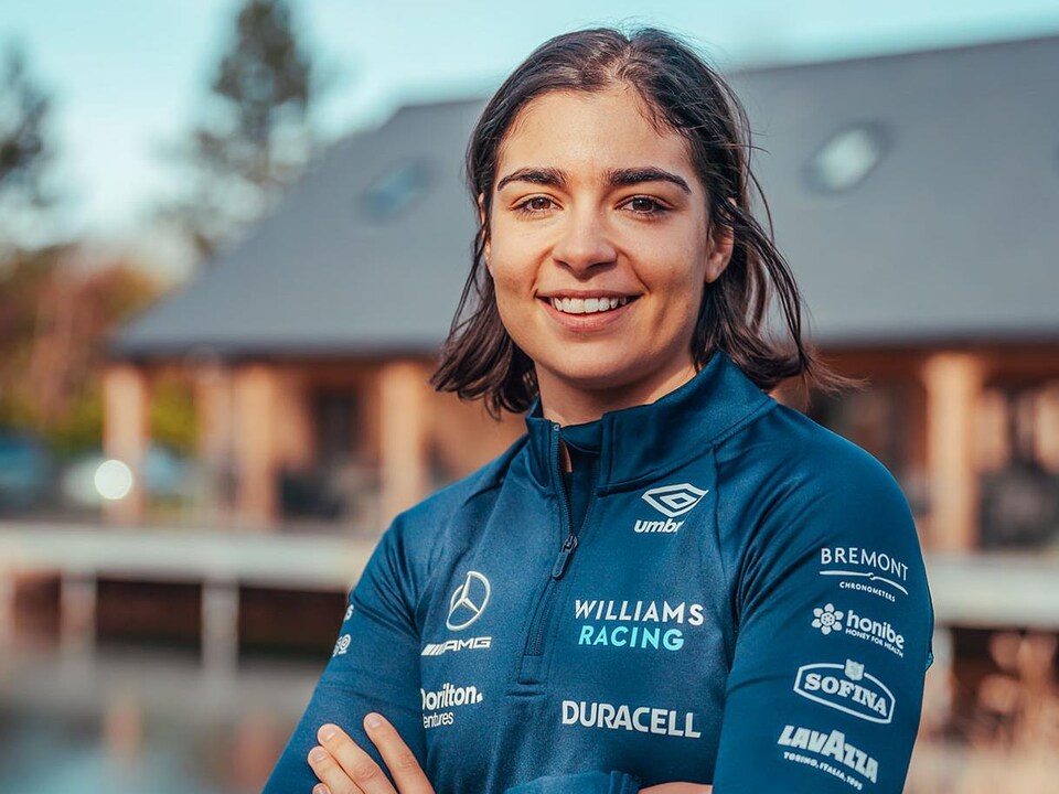 Une jeune femme regarde la caméra et sourit, les bras croisés, dans l'uniforme d'une équipe de F1.