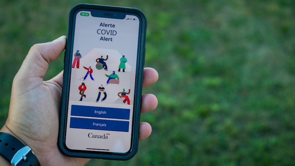 Main qui tient un cellulaire affichant l'application Alerte COVID.