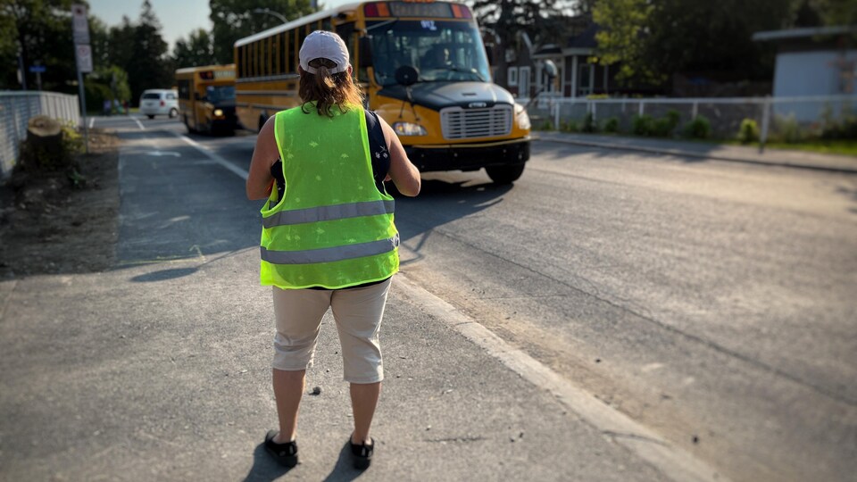 Une personne portant un dossard jaune devant un autobus scolaire.