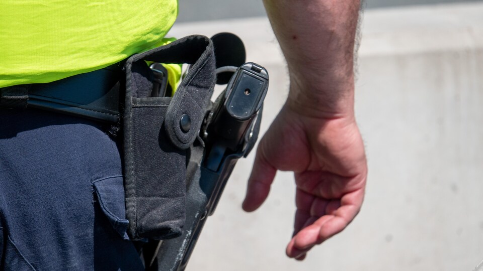 Gros plan sur l'arme à la ceinture d'un policier et de sa main à proximité.