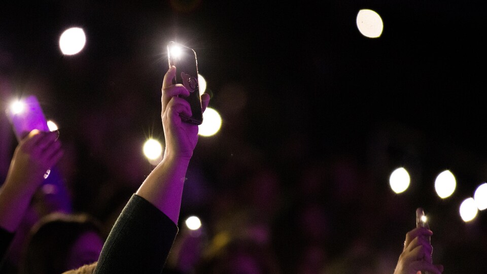 Des bras tendus au cours d'un concert brandissent des téléphones portables dont la lampe torche est activée