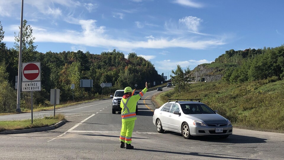 Un individu, vêtu de vêtement de sécurité, contrôle la circulation.