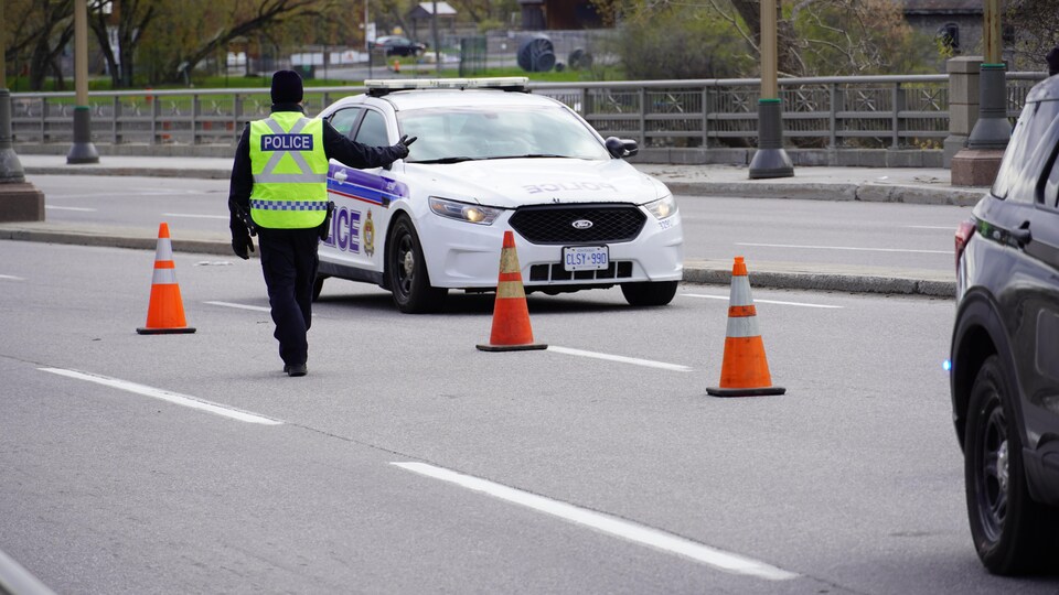 Un policier, sorti de son véhicule, fait signe à un automobiliste.