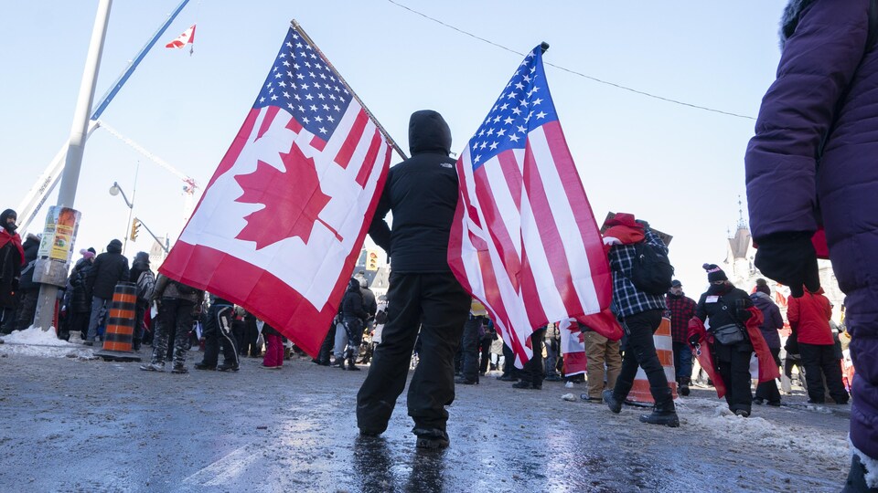 Un manifestant porte un drapeau hybride aux couleurs des États-Unis et du Canada.