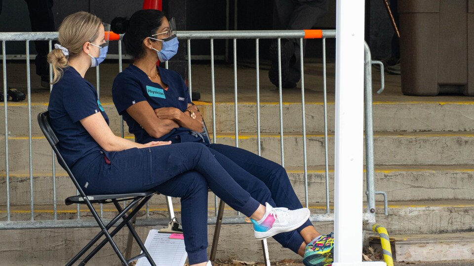 Deux femmes portant le masque chirurgical, sont assises sur des chaises.