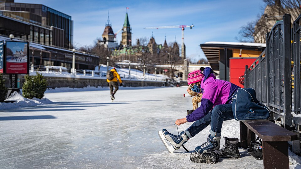 Une femme enfile ses patins sur un banc sur la glace du canal Rideau.