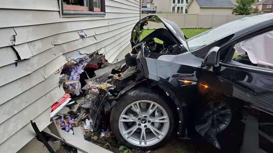 Le devant de la voiture et le mur d'une maison sont lourdement endommagés. 