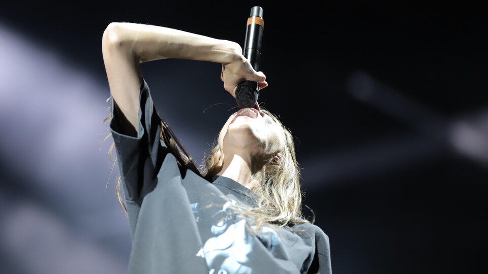 The singer has her head back and holds the microphone in front of her mouth. 