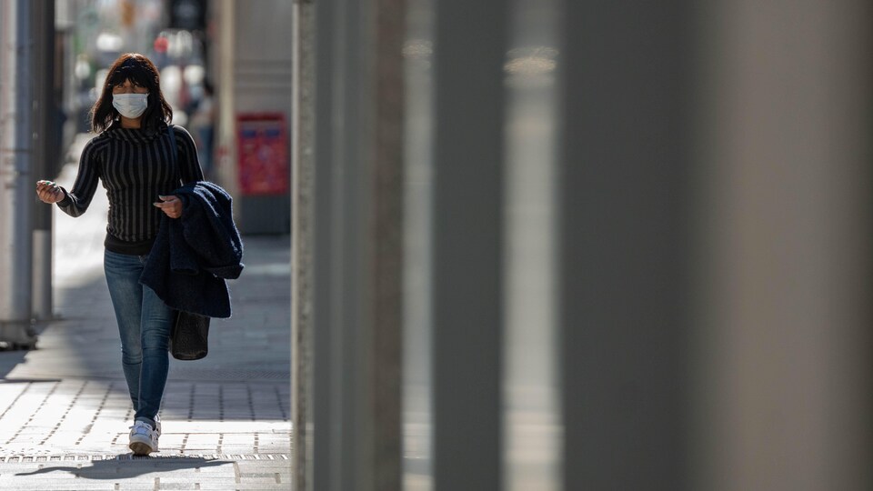 Une personne avec un masque marche dans la rue.