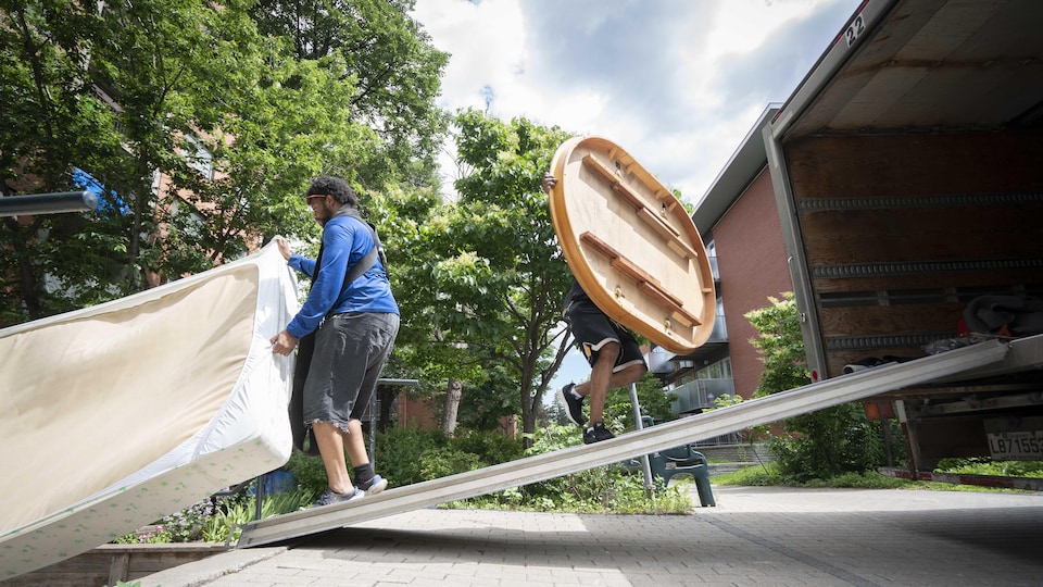 Un homme transporte un matelas et un autre transporte une table ronde à bord d'un camion de déménagement. 