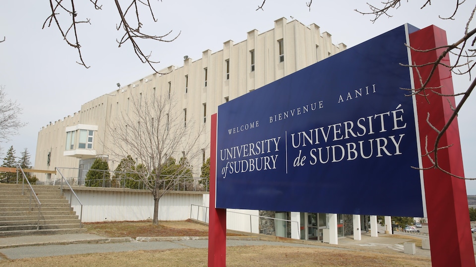 Pancarte indiquant Université de Sudbury à l'extérieur devant un bâtiment.