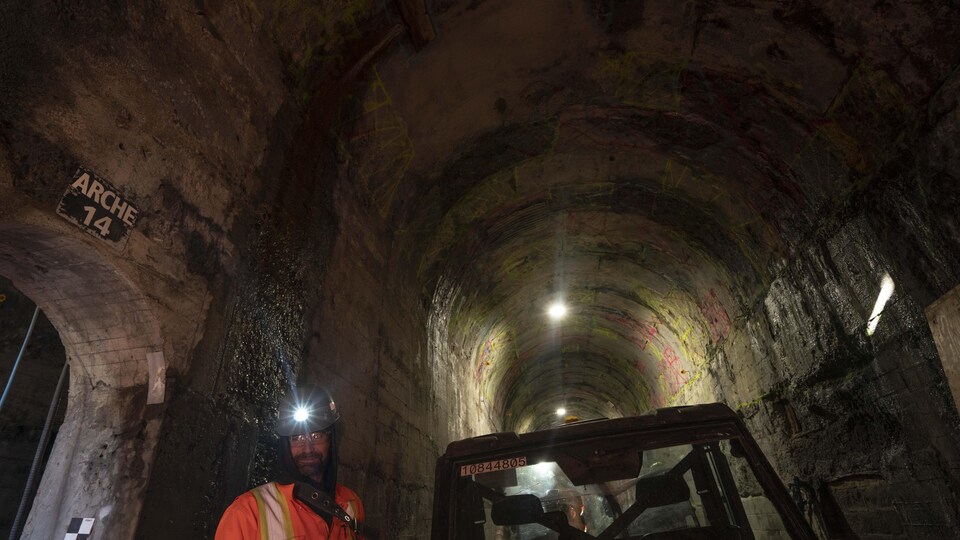 Un ouvrier avec un casque muni d'une lampe frontale dans un vaste tunnel.