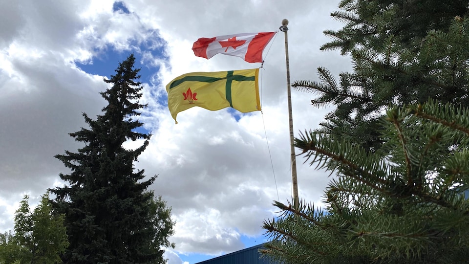 La drapeau canadien et le drapeau fransaskois flottent au vent.