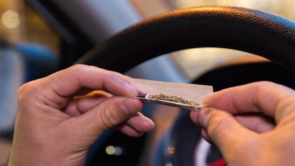 Un homme qui roule un joint de cannabis dans le siège du conducteur d'une voiture.