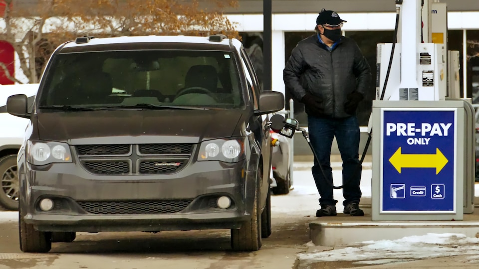 Un homme portant le masque à Regina met de l'essence dans sa voiture.