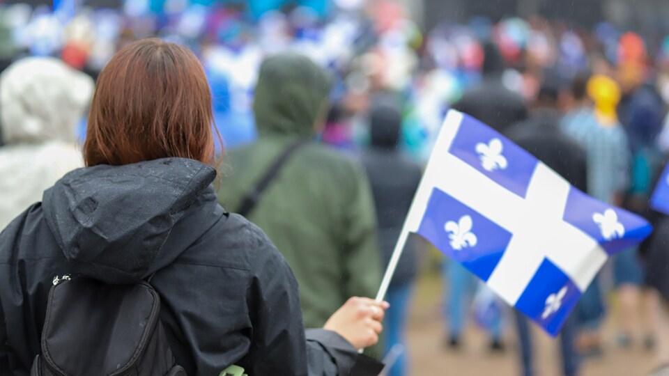 Un dame portant un imperméable de dos avec un drapeau du Québec dans la main droite.