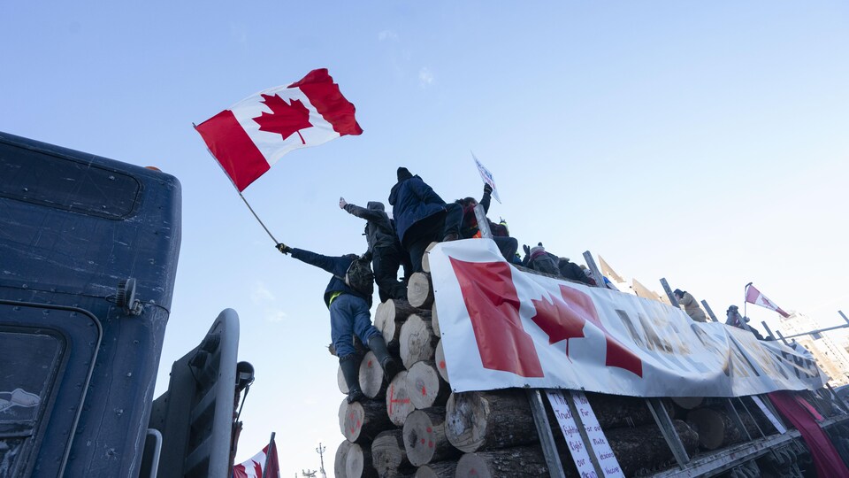 Des gens manifestent et brandissent des drapeaux devant la colline du Parlement, sur la rue Wellington, à Ottawa.