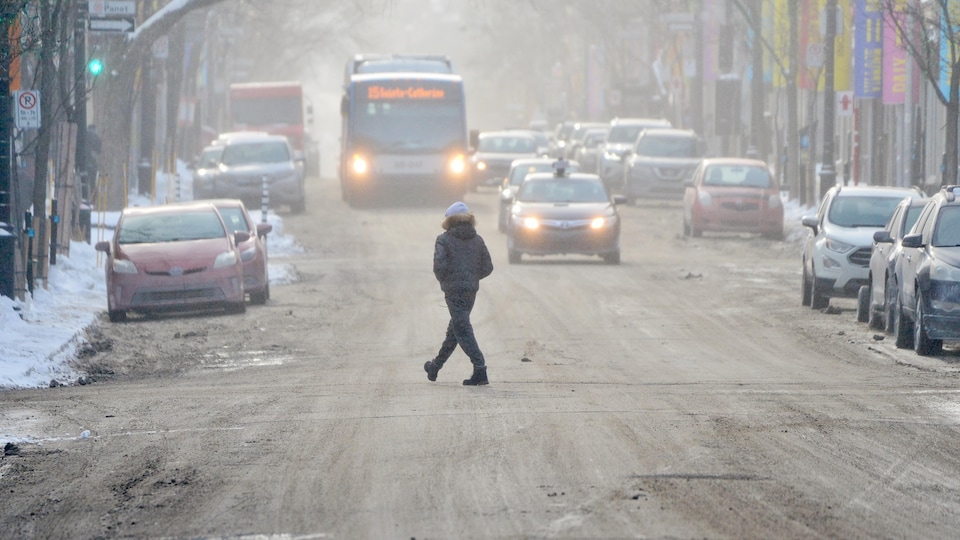 Une personne traverse la rue par un temps d'hiver froid et enneigé.