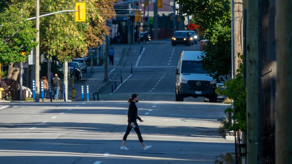 Une piétonne avec un masque traverse une rue.