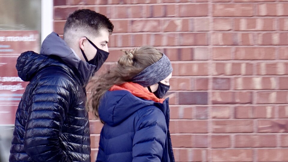 Un homme et une femme, portant un masque sur leurs nez et bouches, marchent ensemble.