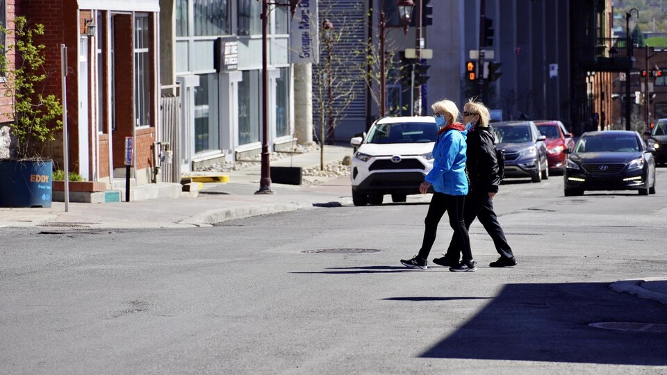 Des piétons portant un masque traversent la rue.