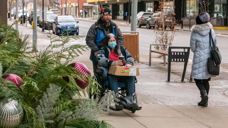 Une personne pousse le fauteuil roulant d'une autre personne et les deux portent un couvre-visage.