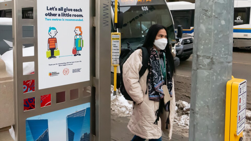 Une personne portant un masque à Regina, en Saskatchewan, marche devant une affiche demandant le respect de la distanciation sociale en raison de la COVID-19.