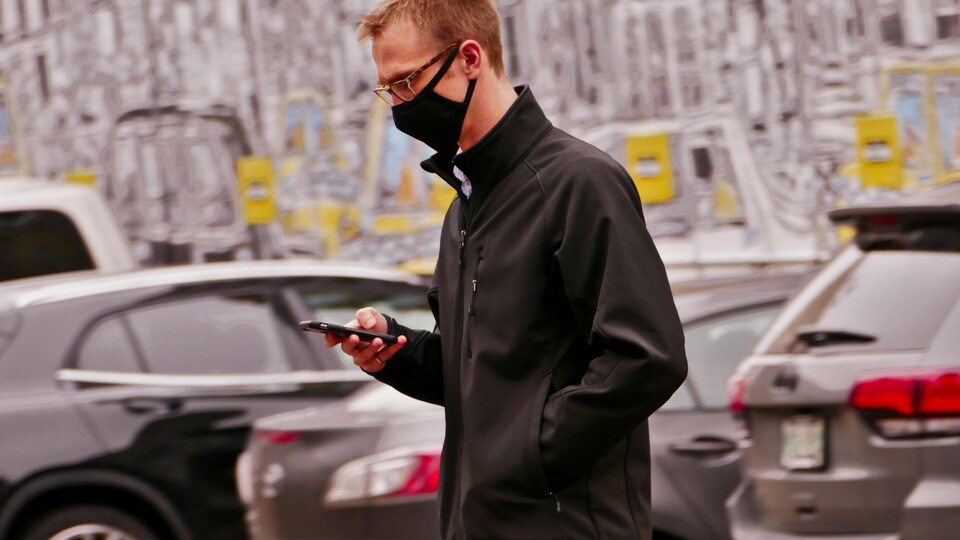 Un homme regarde son téléphone en marchant dehors. (archives)