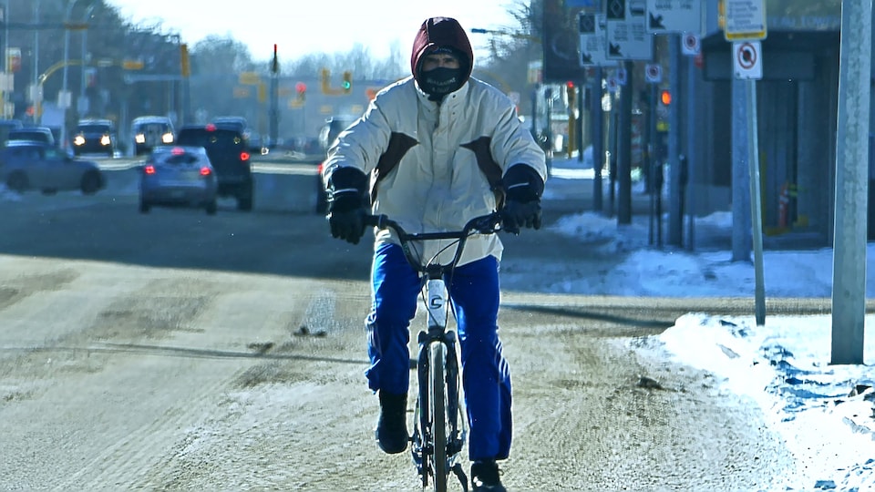 Un homme fait du vélo avec un masque et regarde la caméra de face.