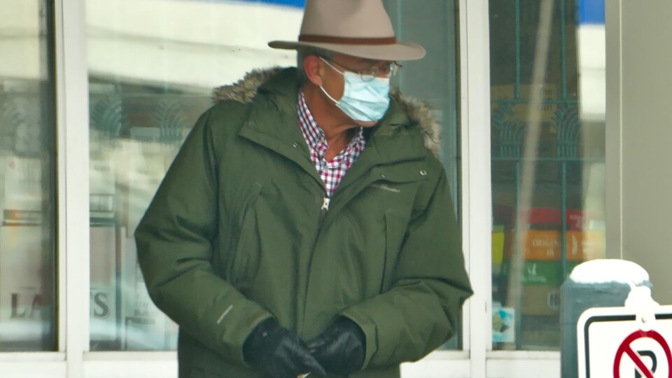 Un passant à fedora marche à l'extérieur, masqué et vêtu d'une parka.