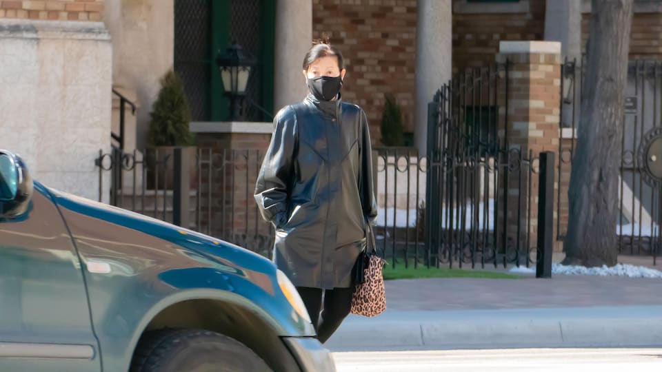 Une femme masquée traverse une intersection piétonnière devant une voiture immobilisée.