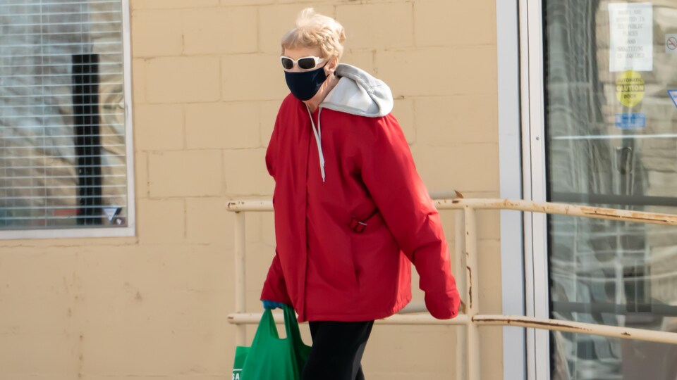 Une femme se promène à l'extérieur avec un masque au visage et un sac à la main
