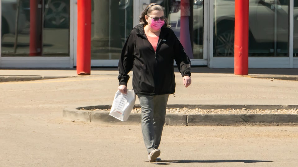 Une femme portant un masque traverse la rue.