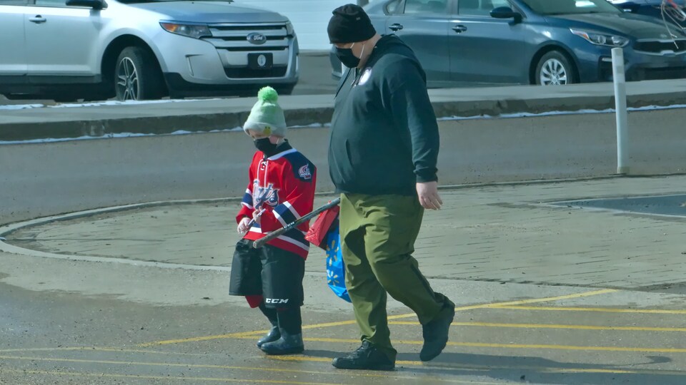 Un homme et un enfant portant tous deux un masque dans un stationnement à Regina, en Saskatchewan.