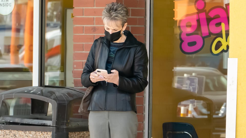 Une femme dans la rue porte un masque en regardant son téléphone.