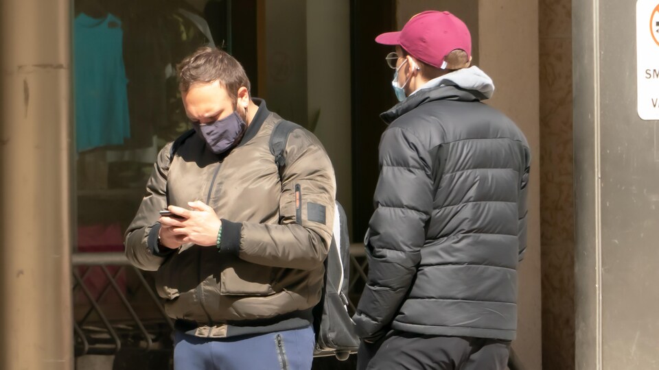Deux hommes portant un masque discutent à l'extérieur.