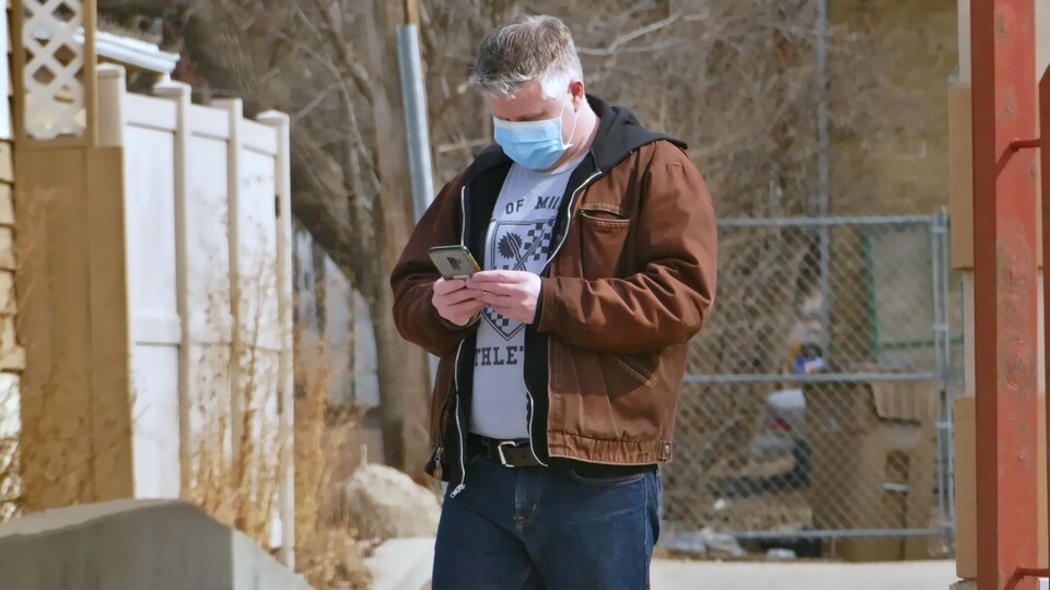 Un homme portant un masque regarde son téléphone.