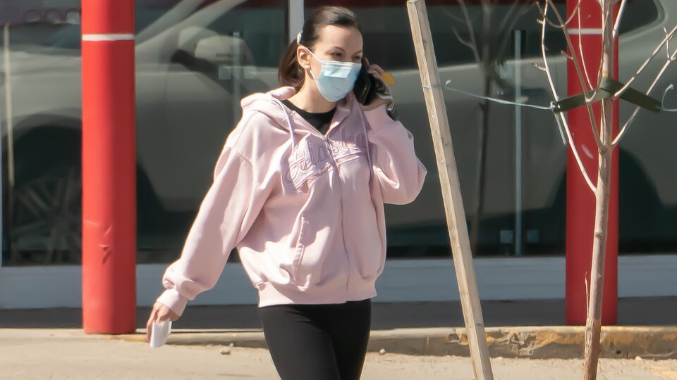 Une femme portant un masque parle au téléphone dans la rue.